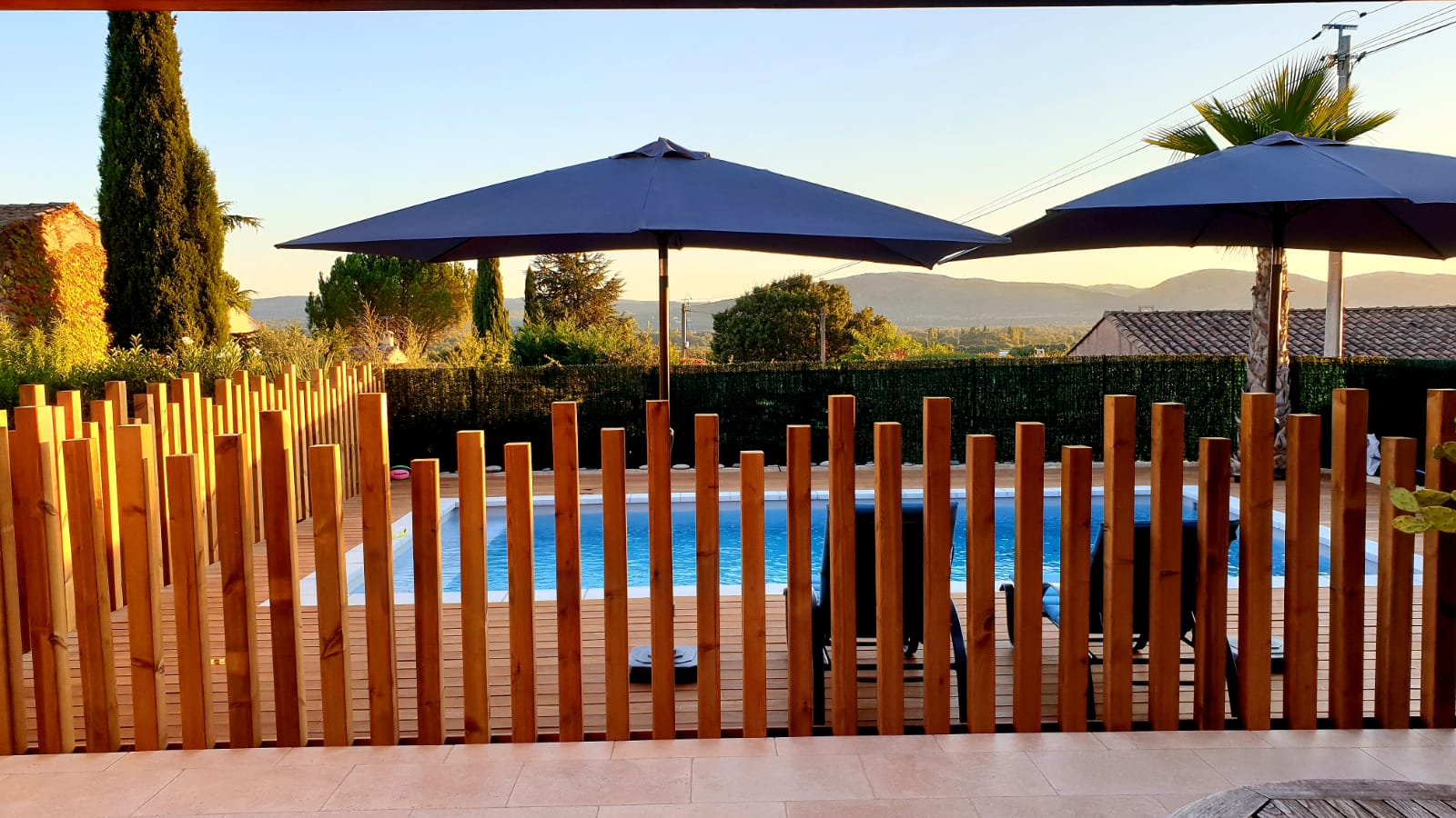 Piscine entourée d'une terrasse en bois, photo prise derrière une barrière en bois